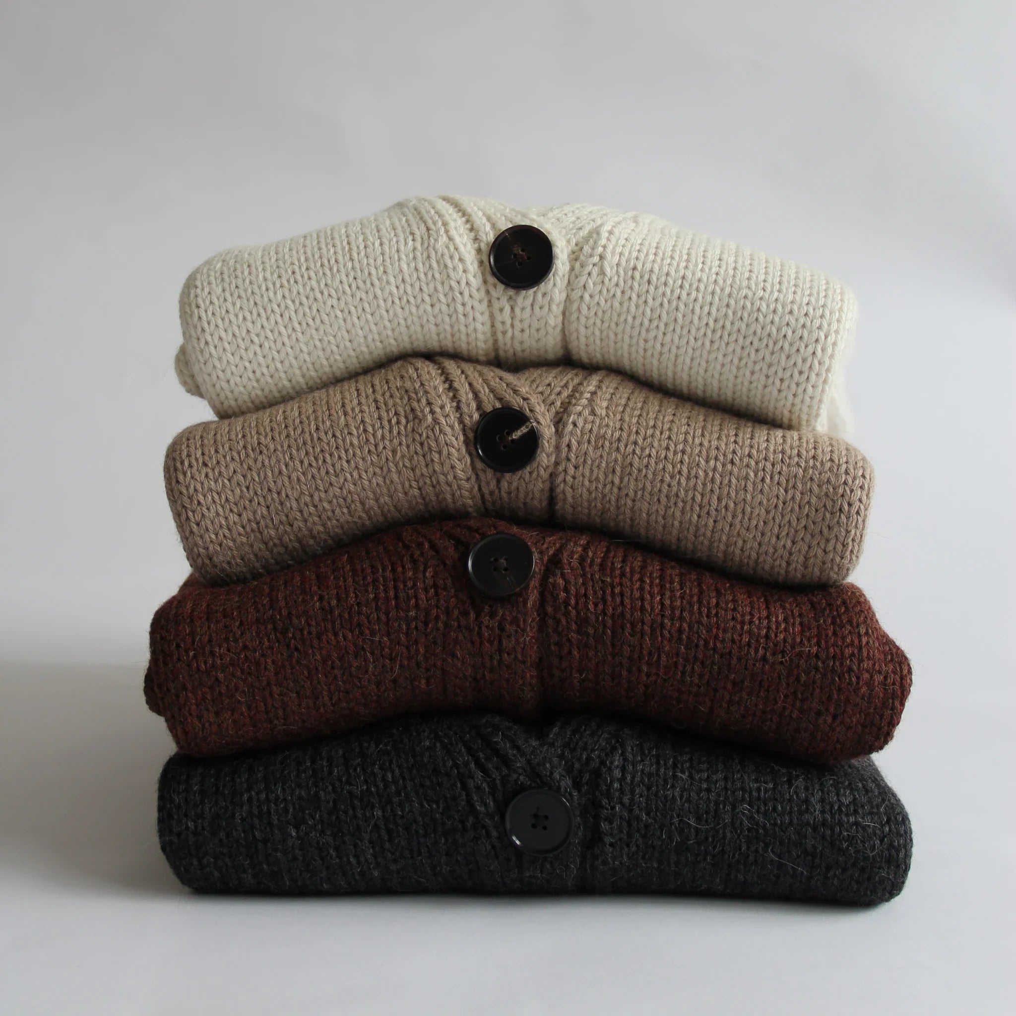 Four 100% Peruvian baby alpaca cardigans in neutral colours folded on top of each other on a white background 