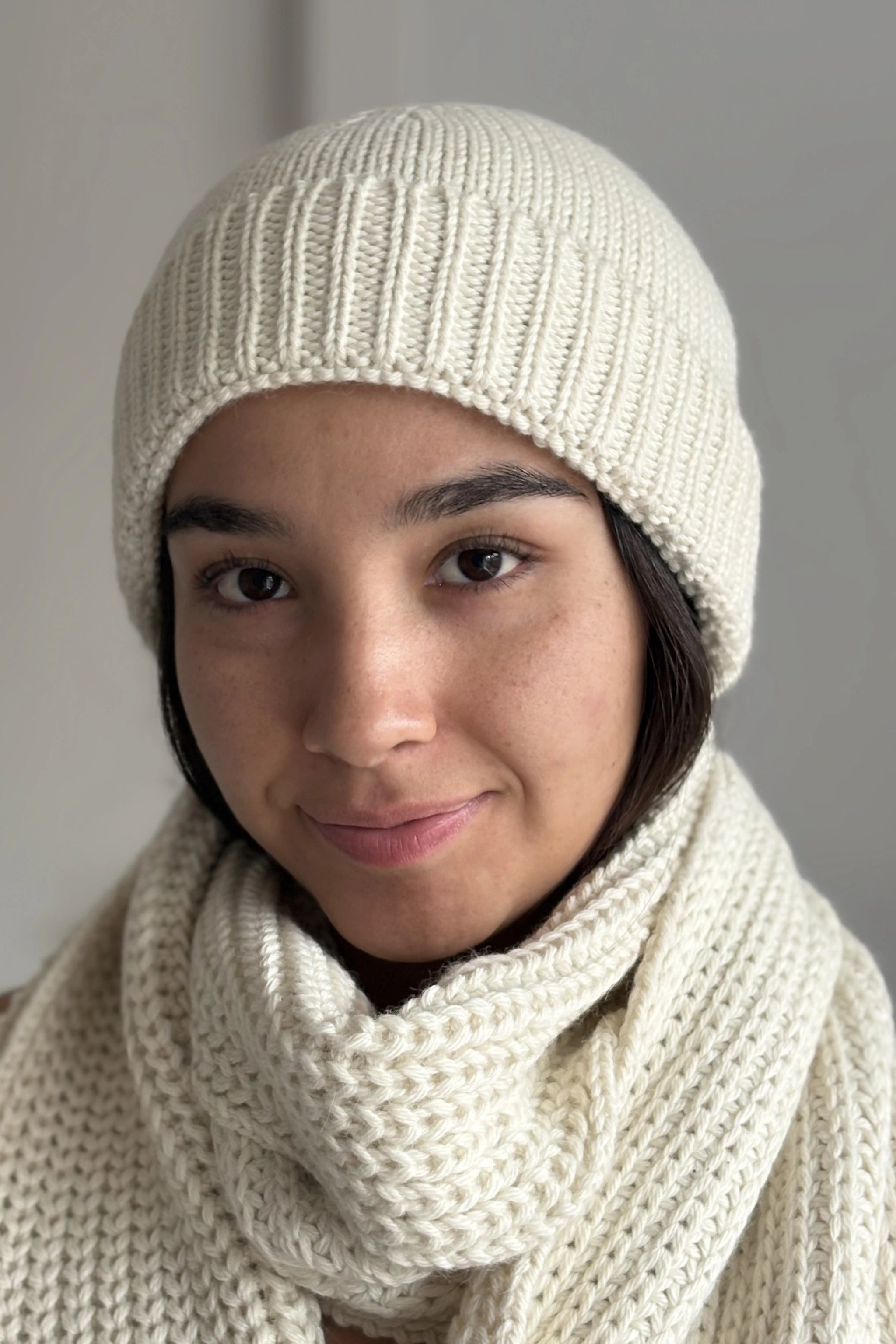 A beautiful young woman wearing a white 100% Peruvian baby alpaca beanie and white baby alpaca scarf with a neutral background 