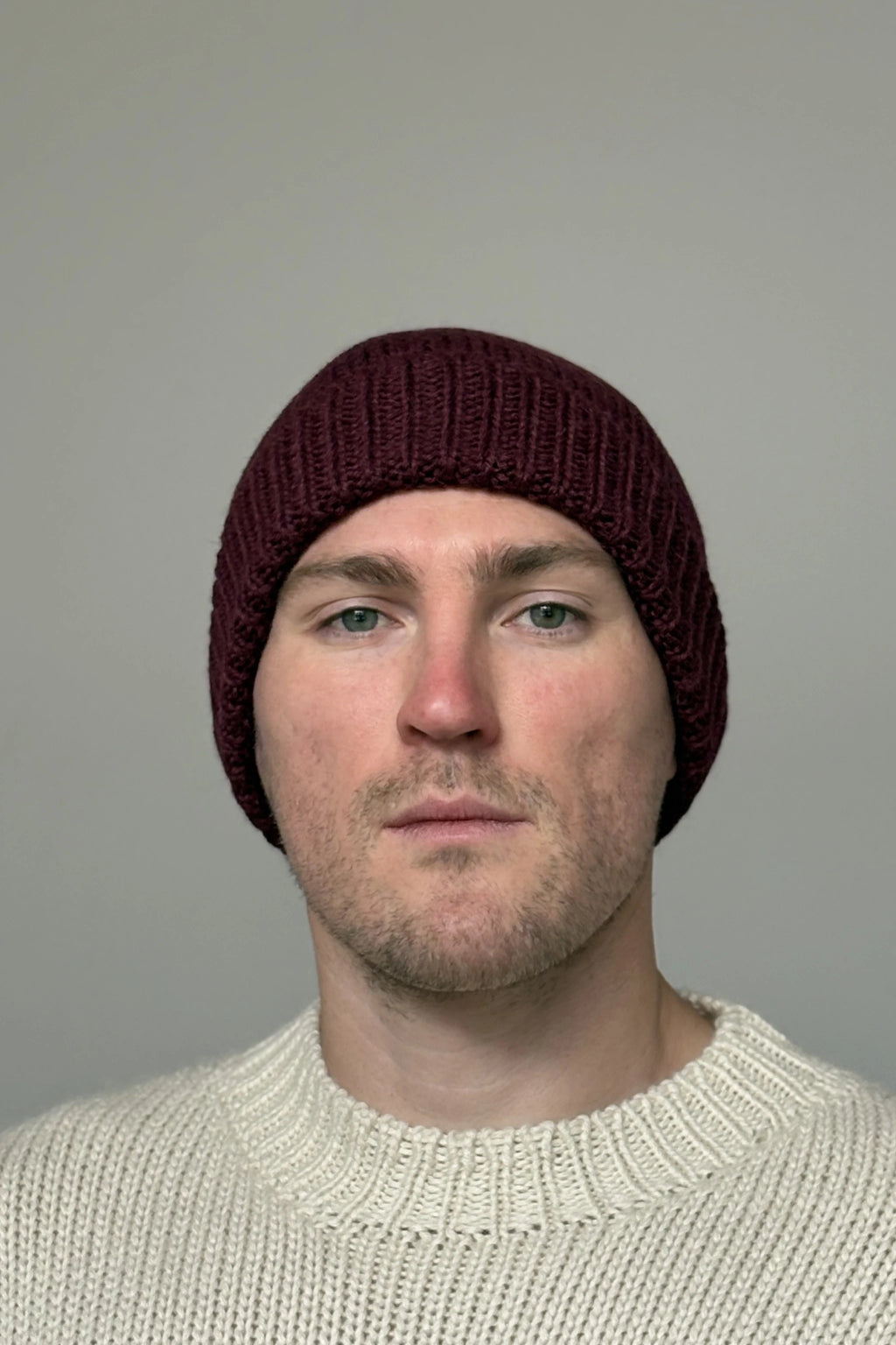 A man wearing a burgundy 100% Peruvian baby alpaca beanie in a white sweater with a neutral background 