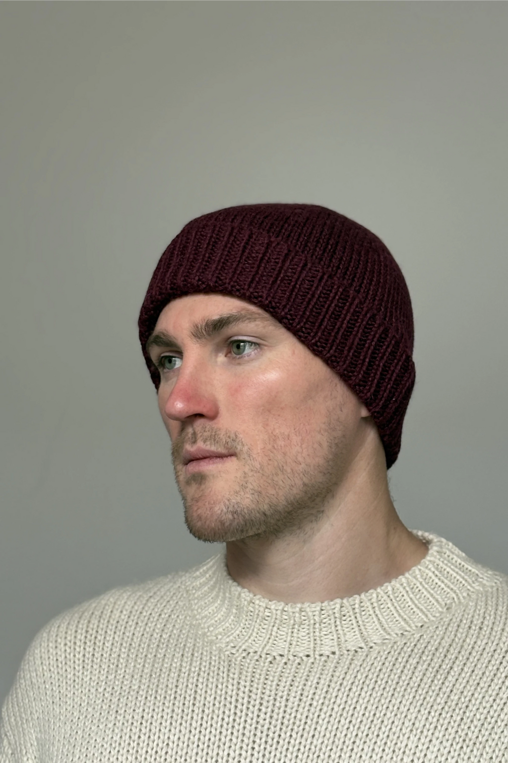 A man wearing a burgundy 100% Peruvian baby alpaca beanie in a white sweater with a neutral background 