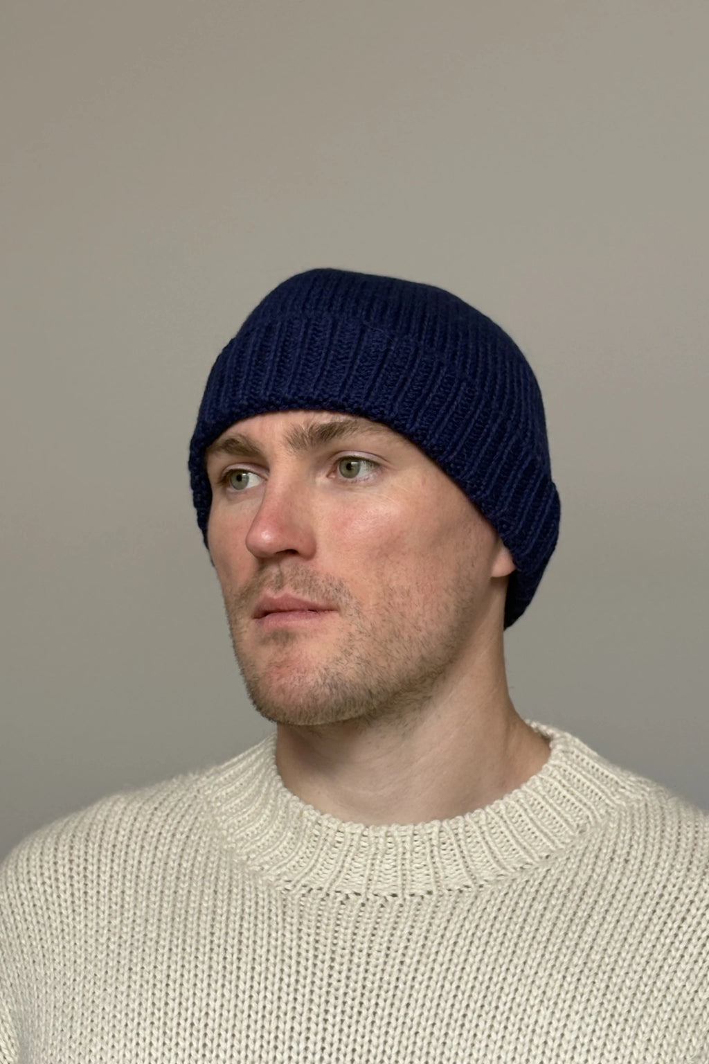 A man wearing a blue 100% Peruvian baby alpaca beanie in a white sweater with a neutral background 
