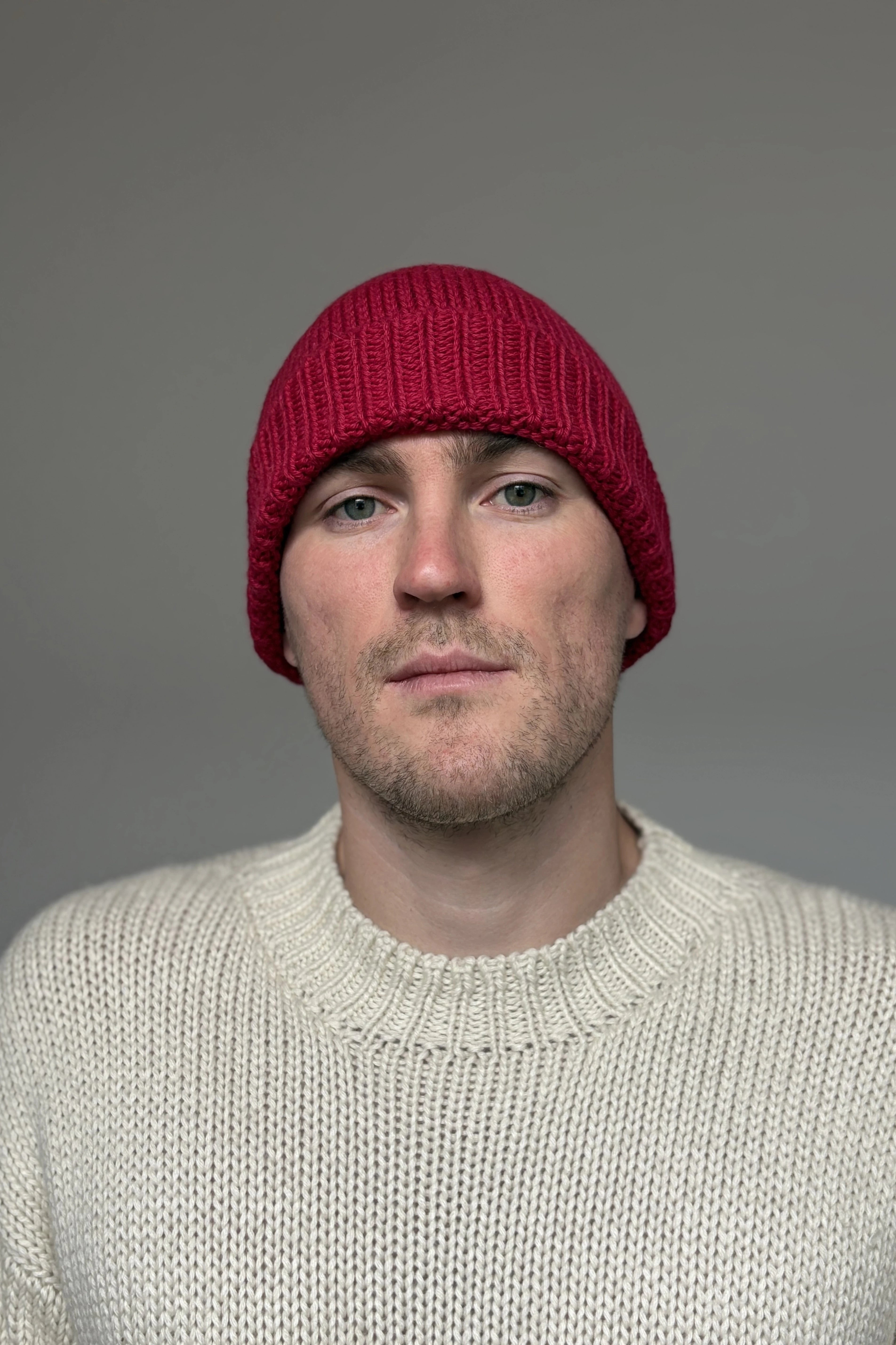 A man wearing a fuchsia 100% Peruvian baby alpaca beanie and a white royal alpaca sweater with a neutral background 