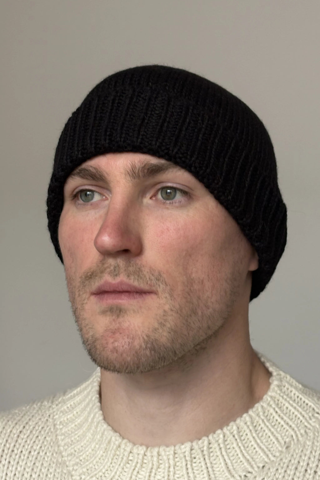 A man wearing a black 100% Peruvian baby alpaca beanie in a white sweater with a neutral background 
