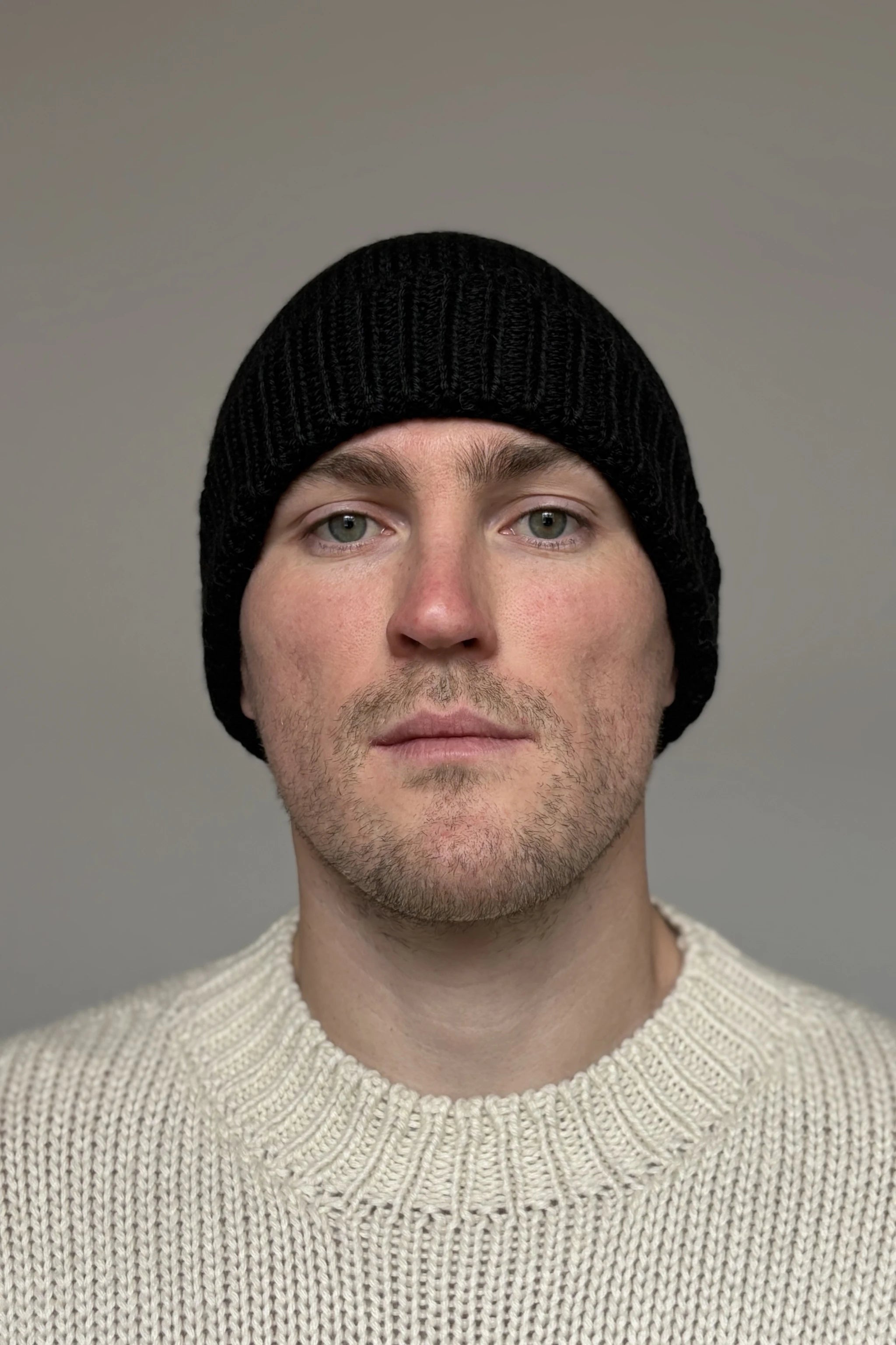A man wearing a black 100% Peruvian baby alpaca beanie in a white baby alpaca sweater with a neutral background 