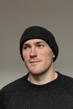 A man wearing a charcoal gray 100% Peruvian baby alpaca beanie and a charcoal gray baby alpaca sweater with a neutral background 