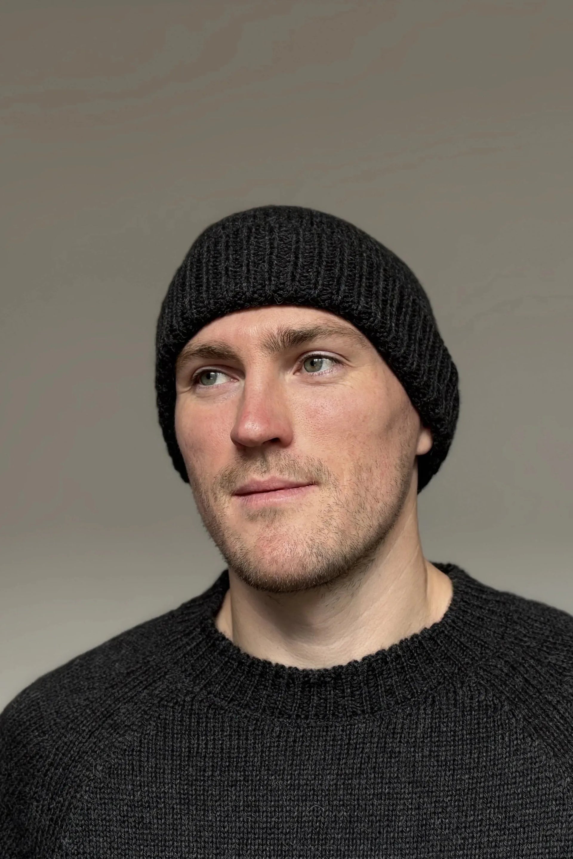 A man wearing a charcoal gray 100% Peruvian baby alpaca beanie and a charcoal gray baby alpaca sweater with a neutral background 