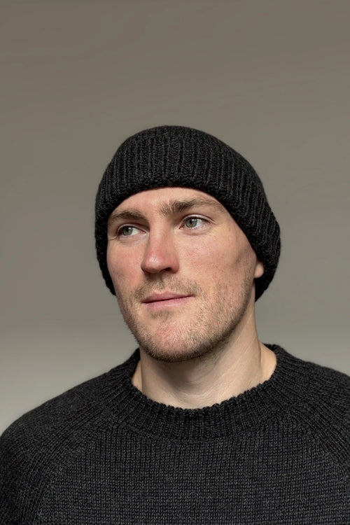 A man wearing a charcoal gray 100% Peruvian baby alpaca beanie and a charcoal gray baby alpaca sweater with a neutral background 