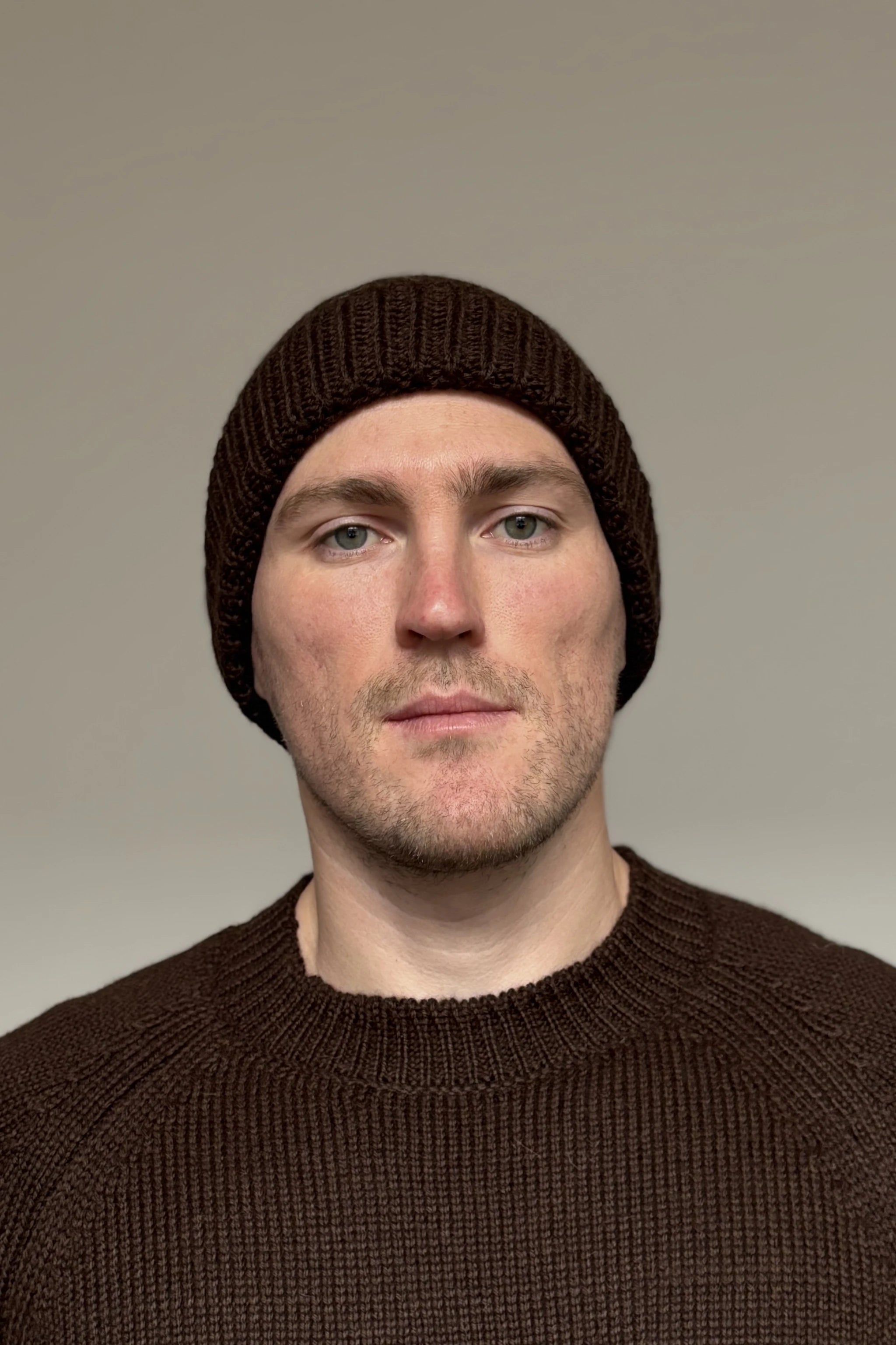 A man wearing a brown 100% Peruvian baby alpaca beanie and a brown baby alpaca sweater with a neutral background 