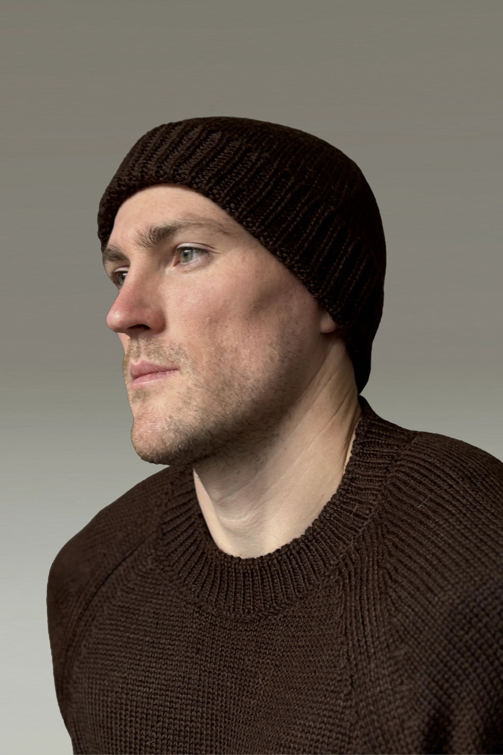A man wearing a brown 100% Peruvian baby alpaca beanie in a brown sweater with a neutral background 