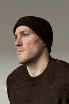 A man wearing a brown 100% Peruvian baby alpaca beanie in a brown sweater with a neutral background 