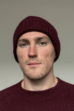 A man wearing a burgundy 100% Peruvian baby alpaca beanie and a burgundy baby alpaca sweater with a neutral background 