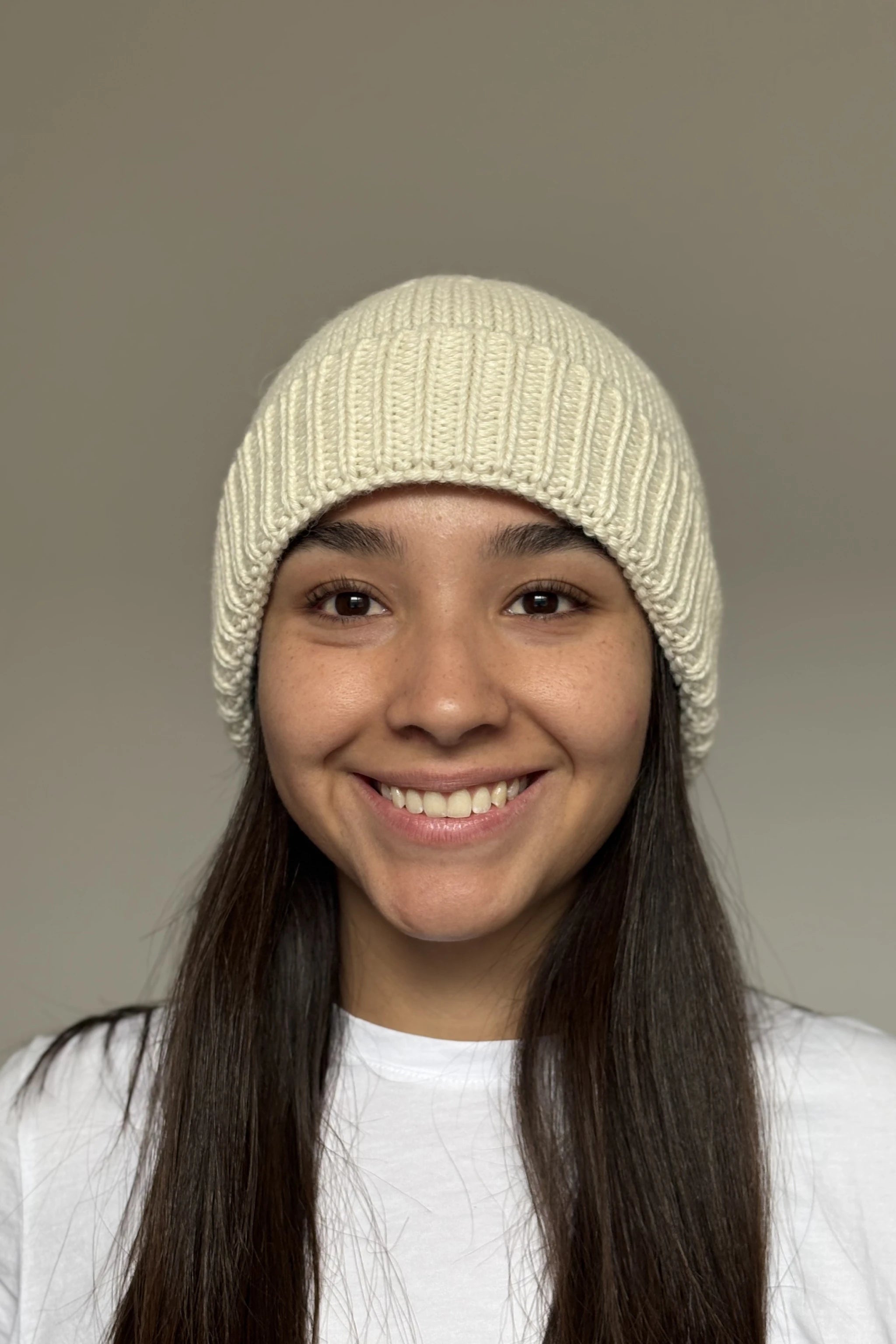 A beautiful young woman wearing a white 100% Peruvian baby alpaca beanie in a white shirt with a neutral background 