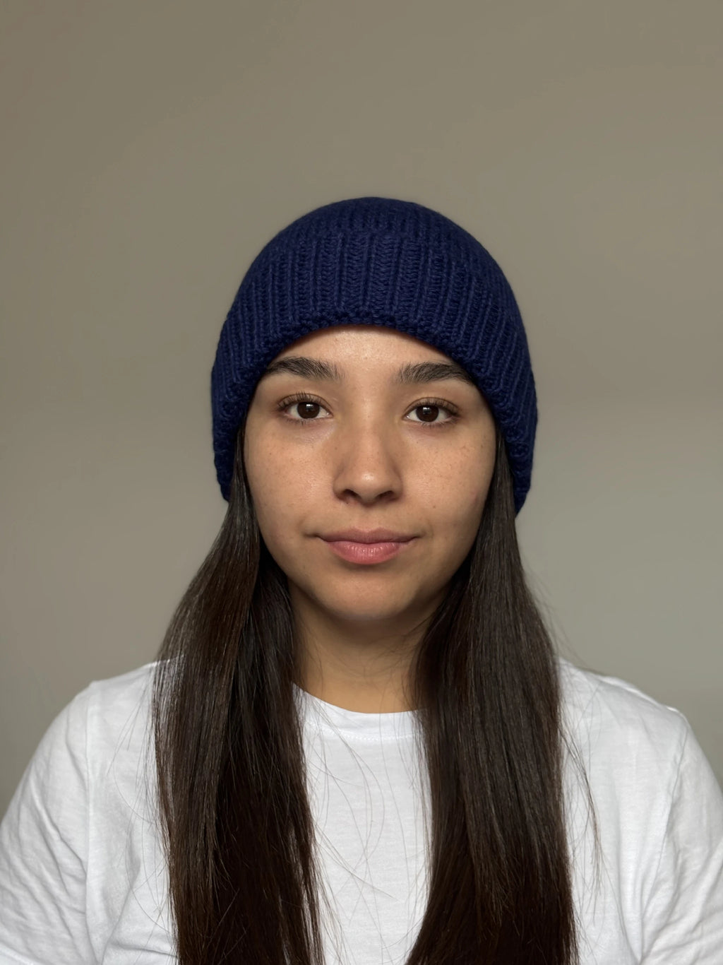 A beautiful young woman wearing a blue 100% Peruvian baby alpaca beanie in a white shirt with a neutral background 