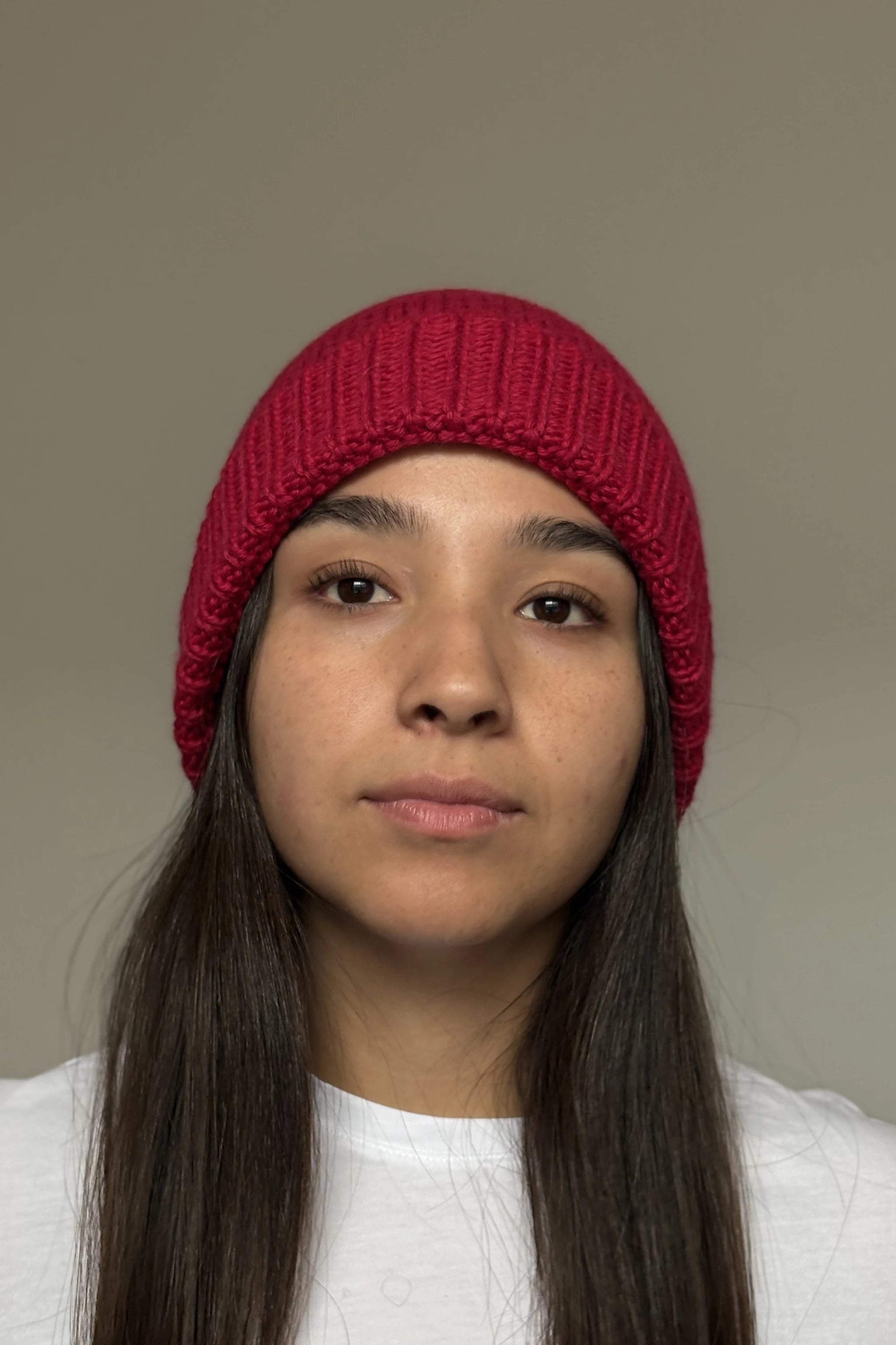 A beautiful young woman wearing a pink 100% Peruvian baby alpaca beanie in a white shirt with a neutral background 