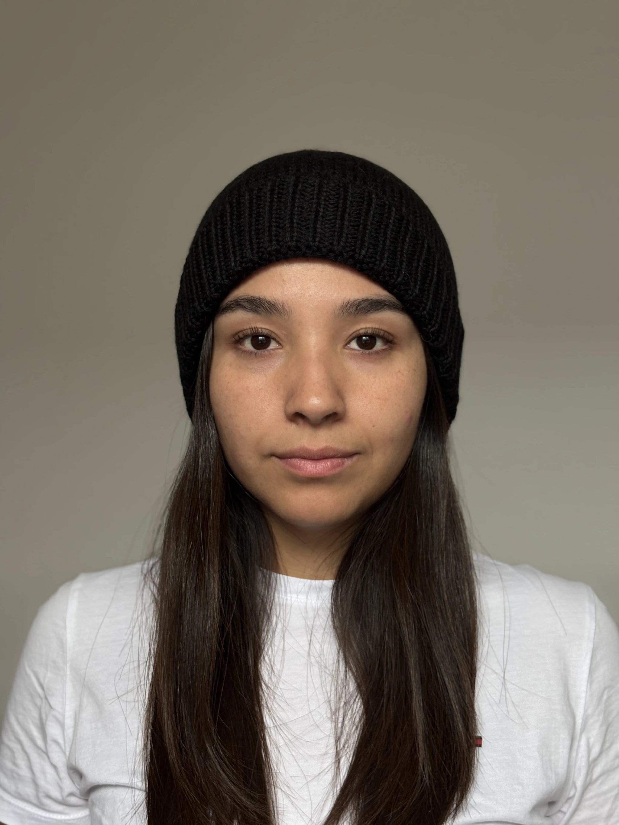 A beautiful young woman wearing a black 100% Peruvian baby alpaca beanie in a white shirt with a neutral background 